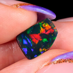 Opal held between fingers showing rich mosaic color from all angles